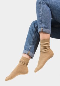 Beżowe skarpetki o prążkowanej fakturze z podwiniętym brzegiem, w połączeniu z dżinsami, prezentujące casualowy styl. Materiał wydaje się miękki i elastyczny.