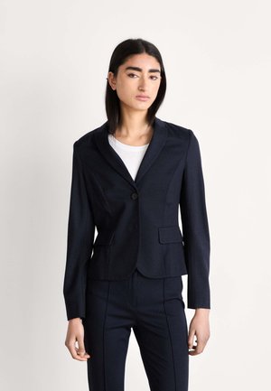 Marineblauwe op maat gemaakte blazer met een enkele knoopsluiting, ingetogene revers, twee voorzakken en een getailleerd silhouette, gecombineerd met bijpassende broeken.