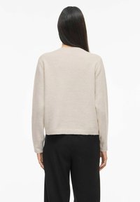 Gaiši bē�ša džemperis ar īsu dizainu, mīkstu tekstūru, garām piedurknēm un ribots apakšmala, kopā ar melnām biksēm.