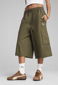 Olivgröna cargoshorts med elastisk midja, sidofickor och sömnadsdetaljer. I kombination med bruna sneakers och vita ankelsockor.