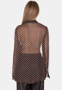 Blusa trasparente marrone con pois bianchi, maniche lunghe e dettaglio cut-out sul retro, caratterizzata da un colletto classico e orlo arrotondato.