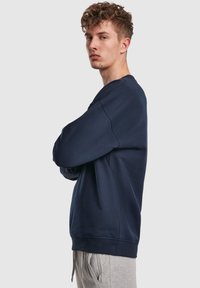 Felpa blu navy in morbido tessuto con vestibilità ampia, scollo rotondo e polsini a costine, abbinata a pantaloni della tuta grigi.