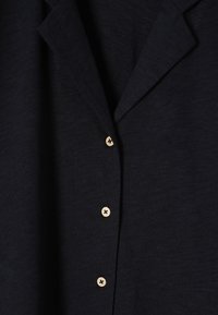 Blazer bleumarin cu o textură netedă, având guler cu decupaj și patru nasturi din lemn deschis pe față.