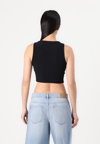 Svart ribbet crop topp med rund halslinning, kombinert med lyseblå high-waisted jeans med baklommer og et merke laget av lær.
