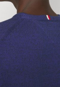 Pullover a maglia testurizzata blu navy con scollatura a costine, caratterizzato da un piccolo accento a strisce rosso, bianco e blu sulla schiena.
