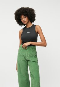 Black sleeveless ribbed tank top with a white logo, paired with high-waisted light green corduroy wide-leg pants.