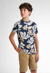 Tmavě modrá krátká košile s květinovým vzorem v krémové a světle modré barvě, doplněná o béžové kraťasy. Košile má kulatý výstřih a běžný střih.