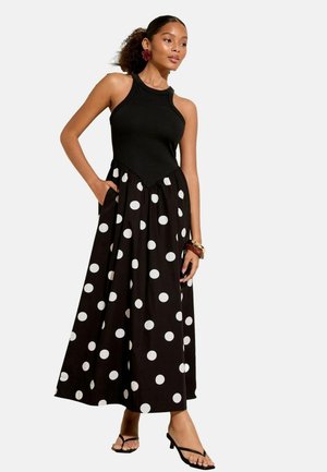 Débardeur noir côtelé associé à une jupe maxi à pois noirs et blancs. Présente des poches latérales et un corsage ajusté. Texture de tissu lisse.