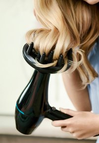 Asciugacapelli nero con un beccuccio rotondo ed allungato e più punte, tenuto vicino ai capelli biondi mossi, con una linea di accento blu.