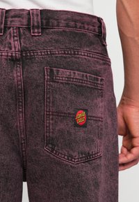 Faded pink denim jeans with a textured finish, featuring a black and red "Santa Cruz" patch on the back pocket.