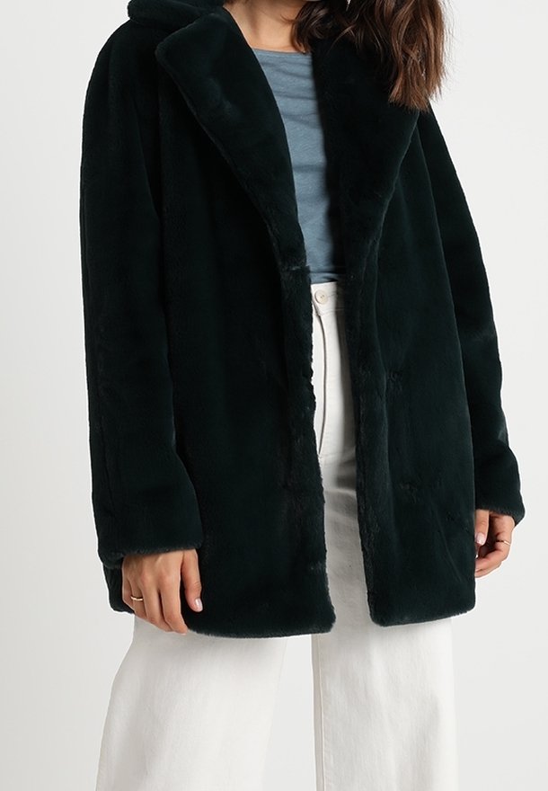 Tummanvihreä tekoturkistakki huivikurilla. Siinä on pitkät hihat, avoin etuosa ja sileä pinta, käytetty vaaleansinisen topin päällä.