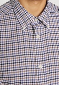 Knapp-up-skjorta med ett flerfärgat rutmönster i bruna, blå och vita nyanser. Tillverkad av vävt tyg med klassisk krage och knappar.