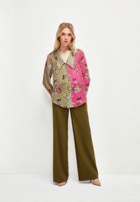 Blusa floreale multicolore con un grande colletto, caratterizzata da sezioni verdi e rosa e una vestibilità ampia, abbinata a pantaloni larghi oliva.