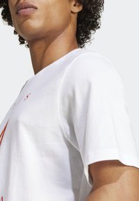 Hvid bomulds T-shirt med korte ærmer og rund halsudskæring, med rød grafisk tekst og designelementer på forsiden.