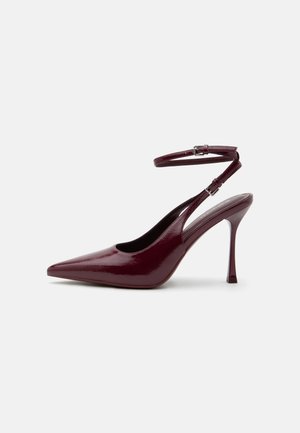 Zapato de tacón alto en burdeos brillante con punta puntiaguda, correa en el tobillo con hebilla, tacón de aguja delgado, vista lateral sobre fondo liso.