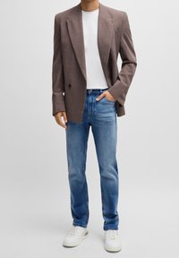 Brun texturerad blazer över en vit t-shirt, tillsammans med ljusblå denimjeans och vita sneakers med subtila detaljer.