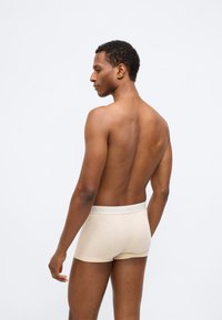 Μπεζ βαμβακερά σλιπ με μαλακή ελαστική μέση, απεικονιζόμενα από πλάγια άποψη σε μοντέλο με κοντά σγουρά μαλλιά, σε απλό φόντο.