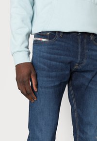 Mörkblå denimjeans med en något avsmalnande passform, med gula sömmar, fem fickor och en etikett på midjebandet.