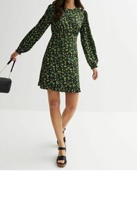 Zwart bloemen mini-jurkje met lange pofmouwen, met groene en gele bloemenpatronen, een aansluitend lijfje en een uitlopende zoom.