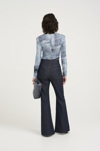 Maglia a maniche lunghe, di colore azzurro chiaro con dettagli arricciati, abbinata a jeans a zampa d'elefante di colore blu scuro. Tiene una borsa grigia. Design semplice e moderno.
