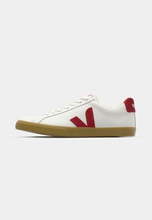 Vita sneakers med röda detaljer, med gummisulor, snörningsdesign, stor röd "V" logotyp på sidan och en slät textur.