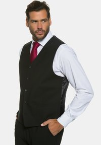 Schwarze Weste mit glatter Textur, ausgestattet mit einem Frontverschluss mit sechs Knöpfen, mit notched Revers und seitlichen Taschen, getragen über einem weißen Hemd.