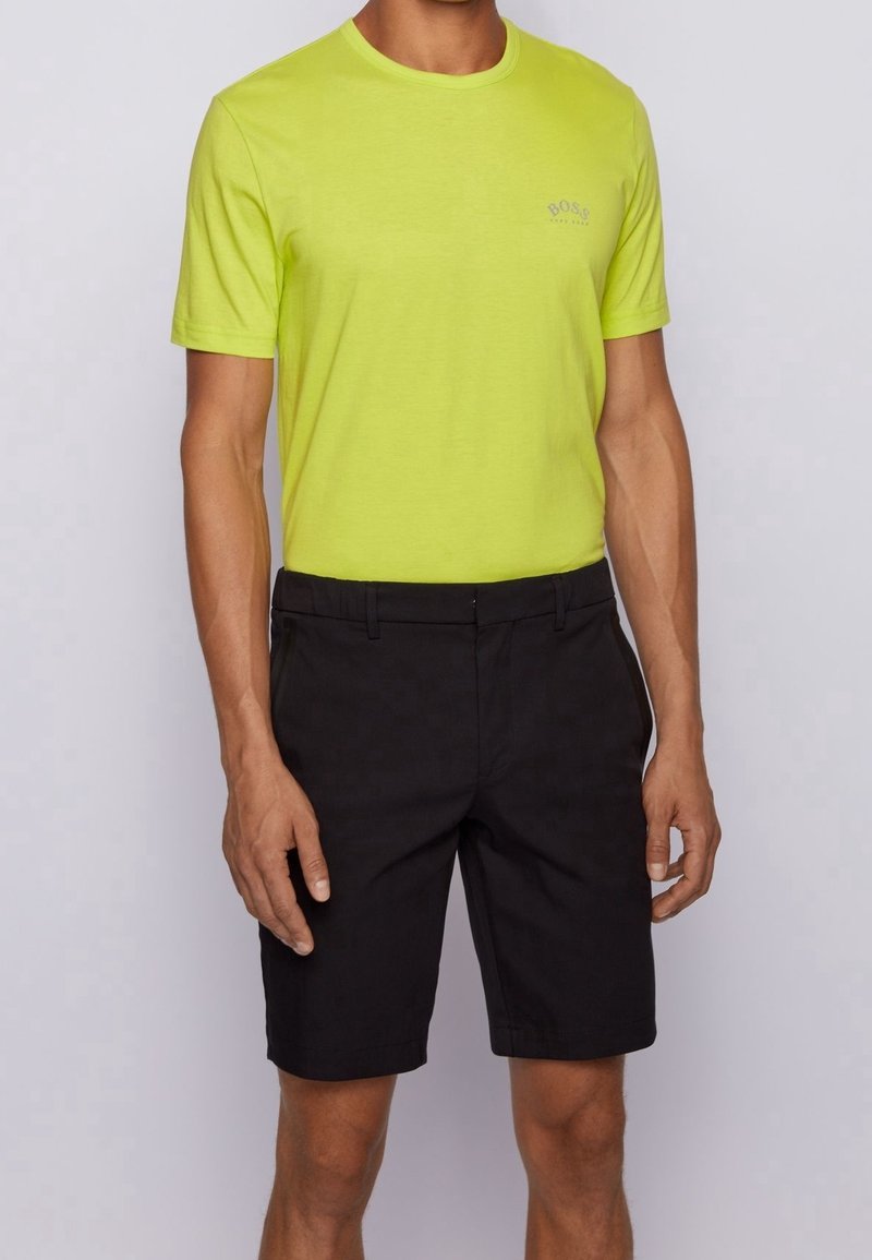 Neon yellow T-shirt with a round neckline and small branding on the chest, paired with black shorts, featuring a flat front and belt loops.