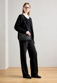 Musta pörröinen neule valkoisen kauluspaidan päällä, yhdistettynä mustiin leveälahkeisiin housuihin. Mustassa olkalaukussa on valkoisia ompelukoristeita.