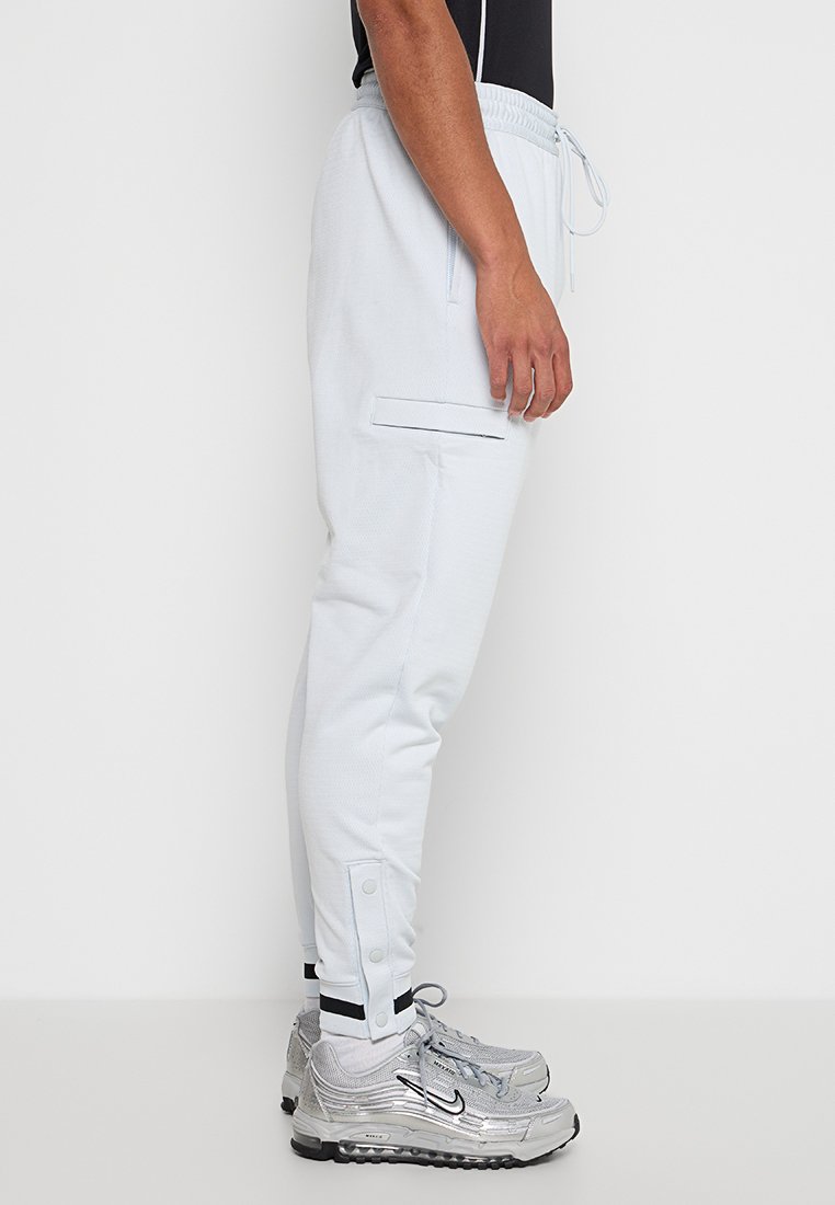 Lichtblauwe joggingbroek van een gladde stof. Beschikt over een elastische tailleband, zijzakken en drukknopen aan de boord.