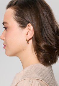 Złote kolczyki koła z małym akcentem w postaci kuli, gładka tekstura i polerowane wykończenie, zaprezentowane na osobie z włosami do ramion.