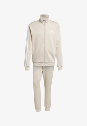 Tuta Adidas beige con giacca con zip e pantaloni coordinati. Caratterizzato da strisce bianche sulle maniche e dettagli con logo su entrambi gli articoli. Tessuto morbido.