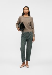 Gai brūnas vilnas džemperis, tumši denima augstās vidukļa bikses, rozā plakanas kurpes un melna rokassoma. Tekstūrēta adījums, brīva piegriezuma, īsas garuma.