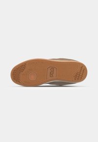 Semelle de sneaker en caoutchouc marron avec un motif de grip texturé, dotée d'une indentation circulaire et d'un détail de logo en relief, le tout sur fond blanc.
