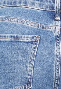 Tela de mezclilla azul con un ligero desgaste, que presenta un bolsillo trasero y costuras en contraste a lo largo de las costuras para mayor durabilidad.