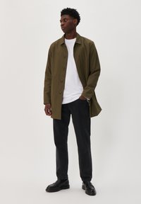 Olíva zöld, könnyű esőkabát gombokkal, fehér pólóval és fekete farmernadrággal párosítva, fekete cipőkkel kiegészítve. Egyszerű design.