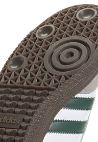 Brun gummisul med ett strukturerat greppmönster som har triangulära utstickare, cirkulära detaljer och gröna och vita ränder på sidan.