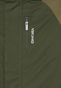 Olīvu zaļa jaka ar rāvējslēdzēja kabatu, "VIKING" logo baltā krāsā, teksturēta auduma, ar kontrastējošiem brūniem akcentiem.