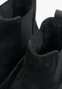 Black suede ankle boots featuring elastic side panels, a soft interior lining, and a textured finish with seamless construction.