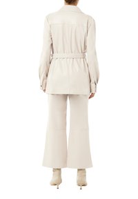 Beżowy płaszcz z paskiem, o zwiewnym kroju, wysokim kołnierzu i długich rękawach, w połączeniu z beżowymi spodniami w dzwony i spiczastymi botkami za kostkę.