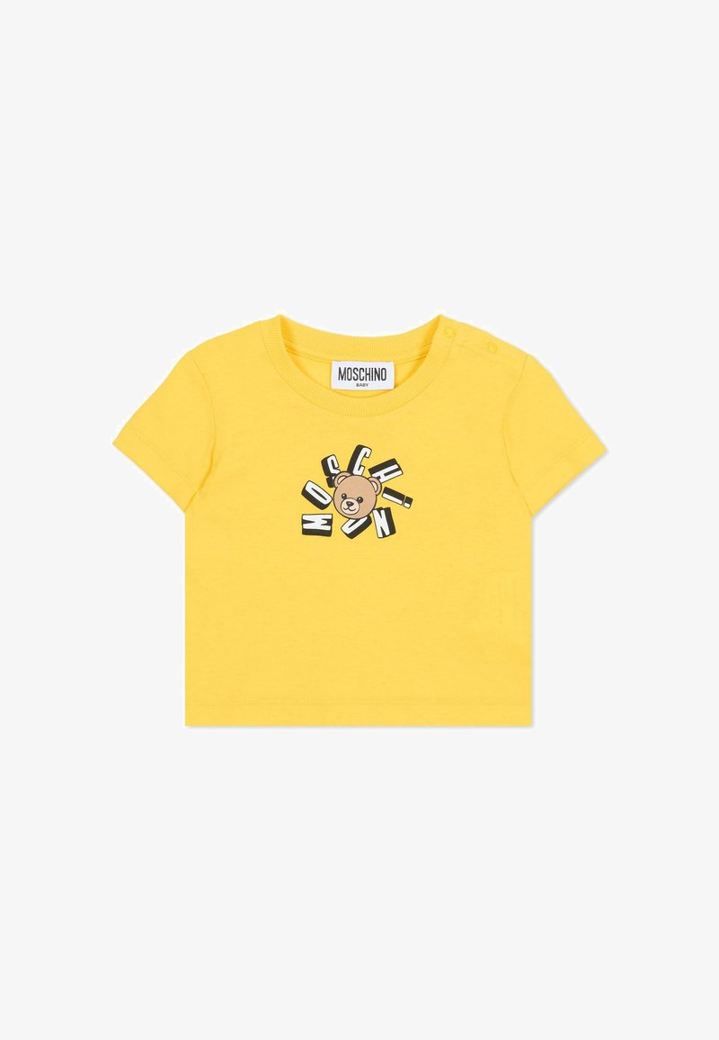Camiseta de algodón amarilla con un gráfico impreso de un oso marrón y el texto "MOSCHINO" en diferentes estilos alrededor; tiene botones a presión en el hombro.