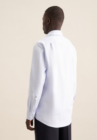 Camicia a maniche lunghe azzurro chiaro con motivo a scacchi, colletto a punta e pieghe sottili sulle spalle. Vestibilità classica con orlo curvo.