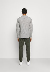 Gray striped long-sleeve shirt with a rounded hem, paired with dark green tapered pants and white sneakers, viewed from the back.