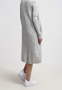 Knälång grå stickad klänning med långa ärmar och ribbade muddar, kombinerad med vita sneakers, mot en neutral bakgrund.