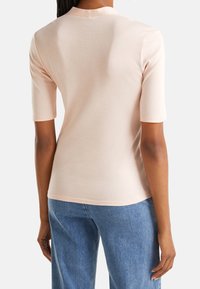 Ljusrosa figurnära topp med korta ärmar, slät textur, rund halsringning och subtila sömnadsdetaljer, i kombination med blå raka jeans.