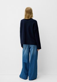 Pull surdimensionné bleu marine avec ourlet côtelé, associé à un jean bleu à jambes larges avec poches arrière et délavé clair.
