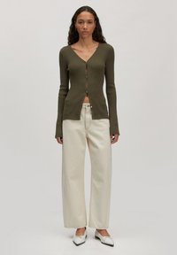 Olivengrüner, gerippter Cardigan mit V-Ausschnitt und Knöpfen, kombiniert mit weiten, cremefarbenen Hosen und weißen Ballerinas mit einer Schleifendetail.