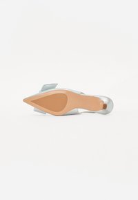 Chaussure à talons argentée avec un bout pointu, finition métallique lisse et une semelle en caoutchouc beige, présentant un accent décoratif au talon.