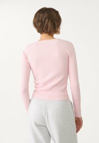 Lichtroze geribd top met lange mouwen en een ronde hals, aansluitend model en een licht korter vallende zoom, gecombineerd met een grijze joggingbroek.