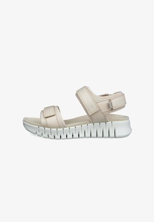Beig sandal med justerbara remmar, med en tjock vit sula med strukturerad design. Slät ovandel med ljusa sömnadsdetaljer.