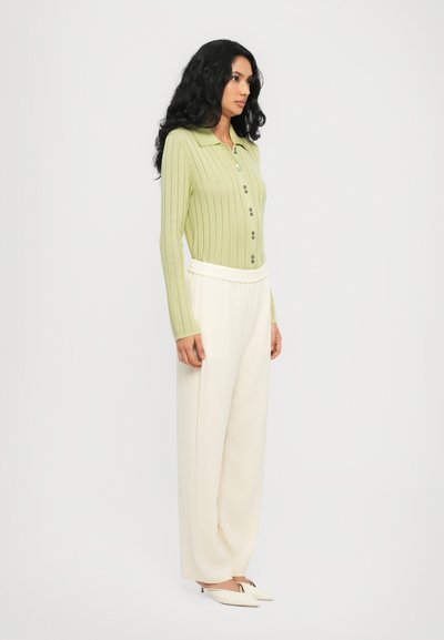 Hellgrüner, langärmeliger gerippter Pullover mit Kragen und Knopfleiste, kombiniert mit lockeren, cremfarbenen Hosen und weißen, hochhackigen Mules.